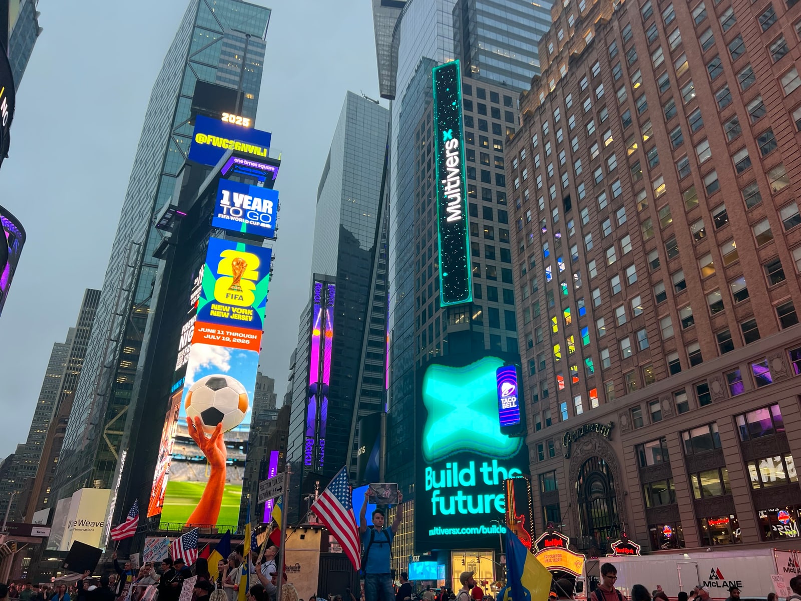 Vertical multi-story MultiversX blockchain brand takeover LED billboard on a Times Square high-rise facade with teal neon border, surrounded by Midtown Manhattan towers