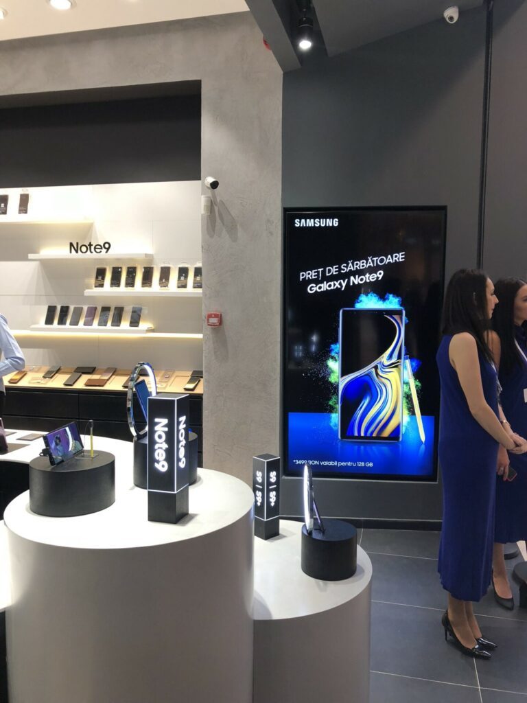 Vertical in-store screen showing the Galaxy Note9 holiday-price creative as visitors stand nearby in the Bucharest store
