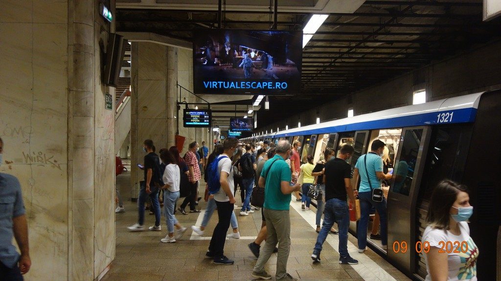 The VIRTUALESCAPE.RO creative running on a digital screen above the platform in Bucharest's Piata Unirii metro station, with commuters and a train passing