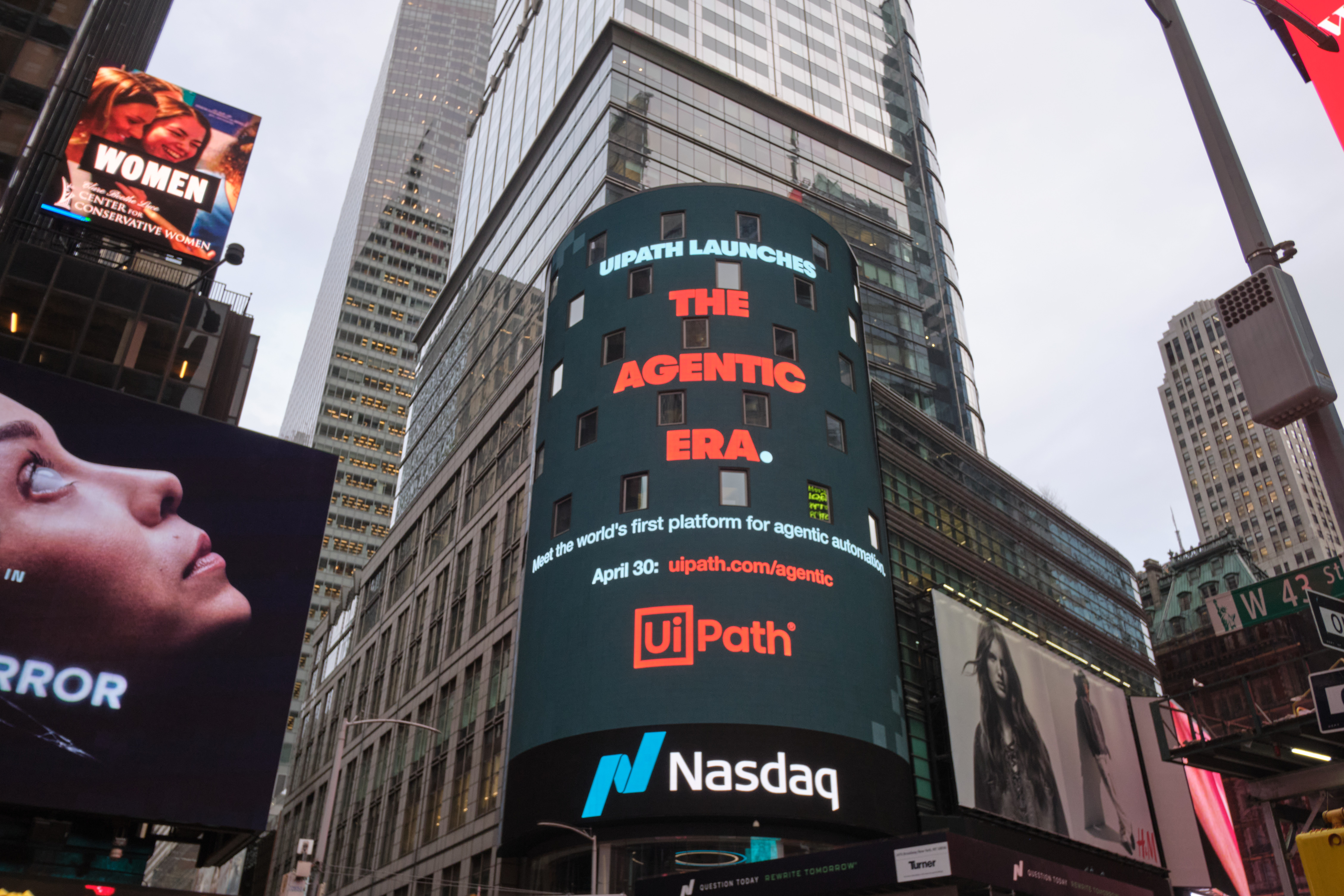 UiPath 'The Agentic Era' product launch campaign wrapped around the Nasdaq tower billboard in Times Square, promoting the world's first agentic automation platform with an April 30 date and uipath.com/agentic URL, surrounded by competing DOOH screens on West 43rd Street in Midtown Manhattan.