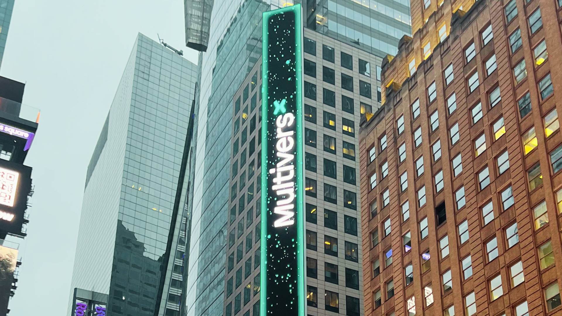 Vertical multi-story MultiversX blockchain brand takeover LED billboard on a Times Square high-rise facade with teal neon border and particle animation, surrounded by Midtown Manhattan glass towers and commercial signage.